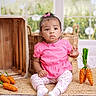 baby, child, pink_clothing, floral_leggings, sitting, decorative_carrots, wooden_basket, woven_mat, indoor, window, garden_background, curly_hair, bow, floor, cute, portrait, expression, natural_light, home_decor, toy