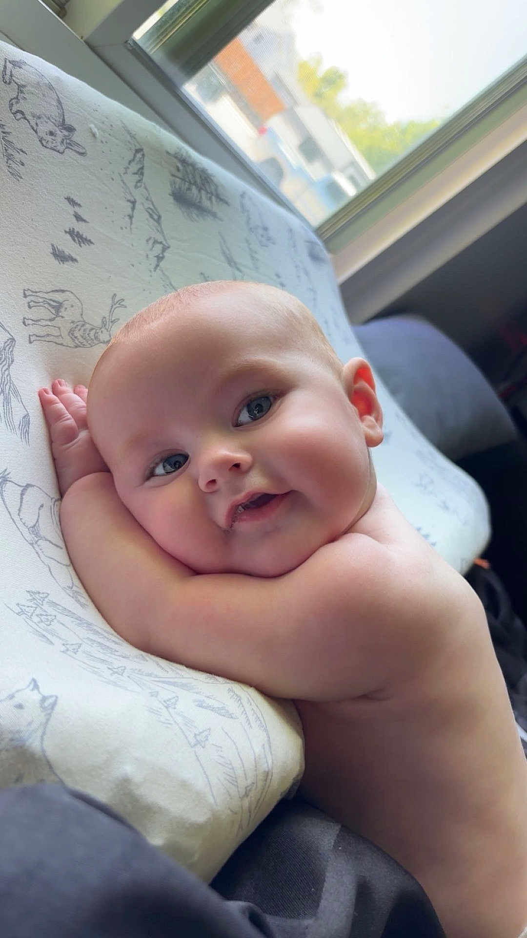 Greyson is registered to the contest to win money with this photo: baby, child, face, smile, cheeks, arm, skin, pillow, window, light, indoors, cute, resting, happy, portrait, infant, expression, natural_light, closeup, sleeping_area