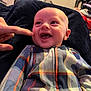Greyson joined the competition — help win amazing prizes! baby, child, smiling, laughing, plaid_clothing, finger, hand, blanket, indoor, cozy, happy, person, infant, cute, cheek, portrait, young_child, warm, playful, closeup