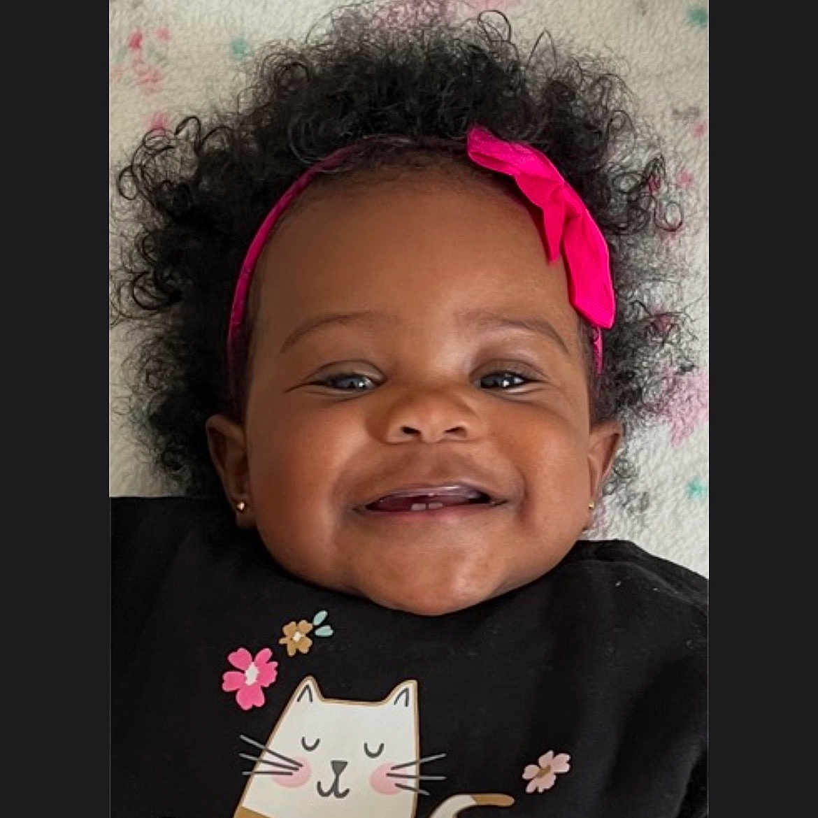 Yessenia joined the competition — help win amazing prizes! baby, smiling, headband, pink_bow, curly_hair, black_shirt, cat_illustration, flowers, cute, portrait, child, happy, earrings, indoor, blanket, closeup, face, infant, apparel, cozy