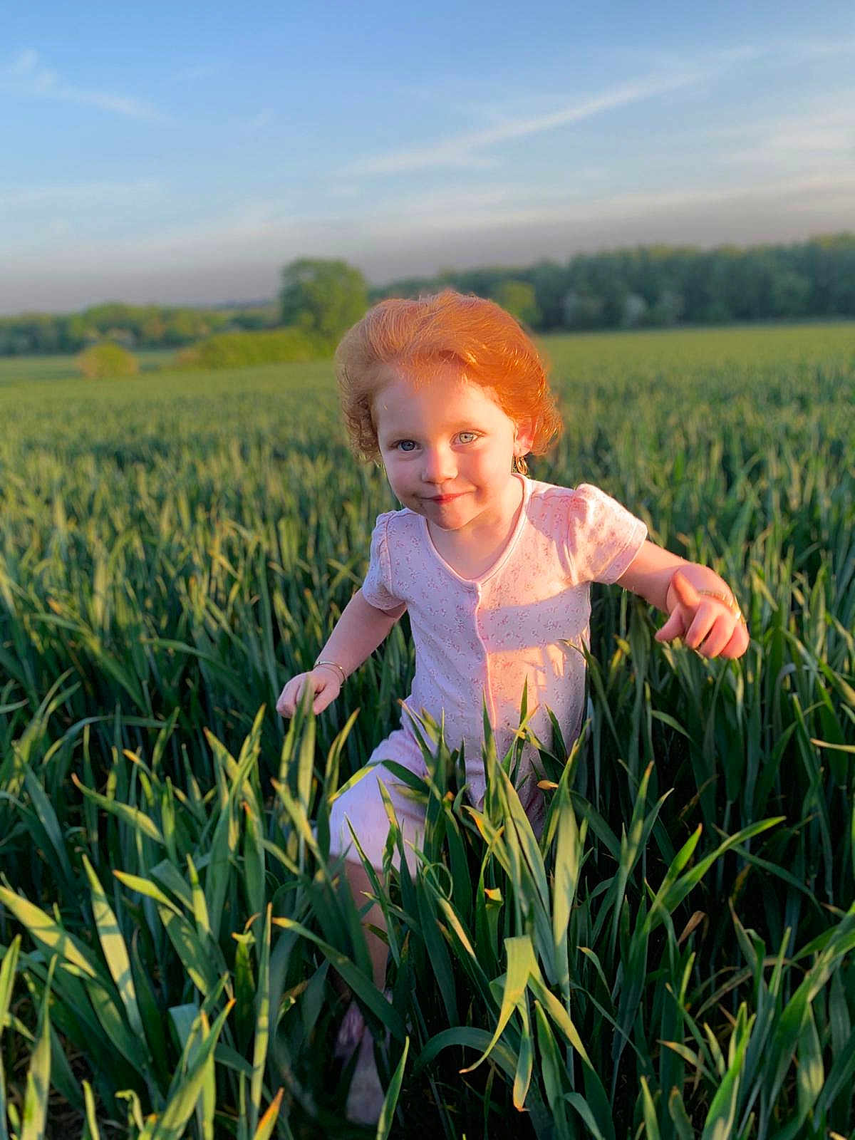 Priscilla is registered to the contest to win money with this photo: child, red_hair, pink_dress, field, greenery, grass, outdoor, sunlight, nature, happy, playful, blue_sky, young_girl, summer, smiling, portrait, daylight, cute, person, environment