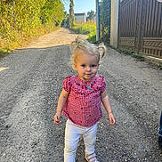 Léna a rejoint le concours — aidez-le/la à gagner de superbes lots ! toddler, child, girl, blonde_hair, pigtails, red_checkered_top, white_pants, pink_shoes, gravel_path, outdoor, sunny, greenery, fence, gate, walking, person, daylight, nature, portrait, casual_clothing