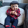 baby, child, plaid_shirt, navy_pants, socks, cap, cushion, smile, hands, face, blue_eyes, indoor, sofa, cozy, cute, portrait, clothing, seated, infant, hat