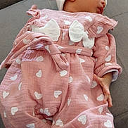 Cataleya a rejoint le concours — aidez-le/la à gagner de superbes lots ! baby, sleeping, infant, pink_outfit, hearts_pattern, white_hat, pom_pom, couch, gray_fabric, cozy, child, peaceful, soft_lighting, indoor, cute, small_hands, footwear, clothing, portrait, resting