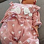 baby, sleeping, infant, pink_outfit, hearts_pattern, white_hat, pom_pom, couch, gray_fabric, cozy, child, peaceful, soft_lighting, indoor, cute, small_hands, footwear, clothing, portrait, resting
