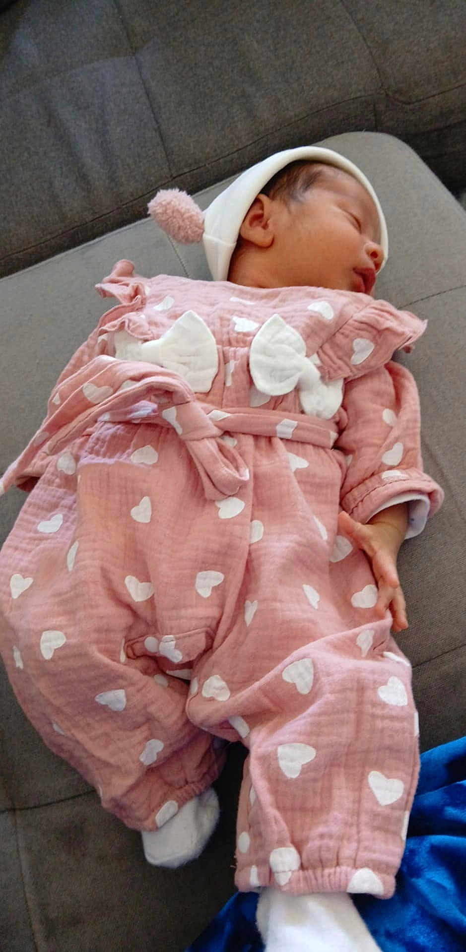 Cataleya a rejoint le concours — aidez-le/la à gagner de superbes lots ! baby, sleeping, infant, pink_outfit, hearts_pattern, white_hat, pom_pom, couch, gray_fabric, cozy, child, peaceful, soft_lighting, indoor, cute, small_hands, footwear, clothing, portrait, resting