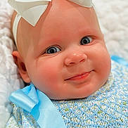 Lynnon is registered to the contest to win money with this photo: baby, infant, face, blue_eyes, bow, headband, smile, dress, blue_ribbon, floral_pattern, soft_blanket, close_up, cute, child, skin, cheeks, portrait, baby_clothing, happy, indoors