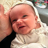 Violett is registered to the contest to win money with this photo: baby, infant, smile, face, hand, onesie, clothing, quilt, soft_fabric, indoor, person, newborn, cute, child, warmth, comfort, happy, portrait, closeup, baby_toys