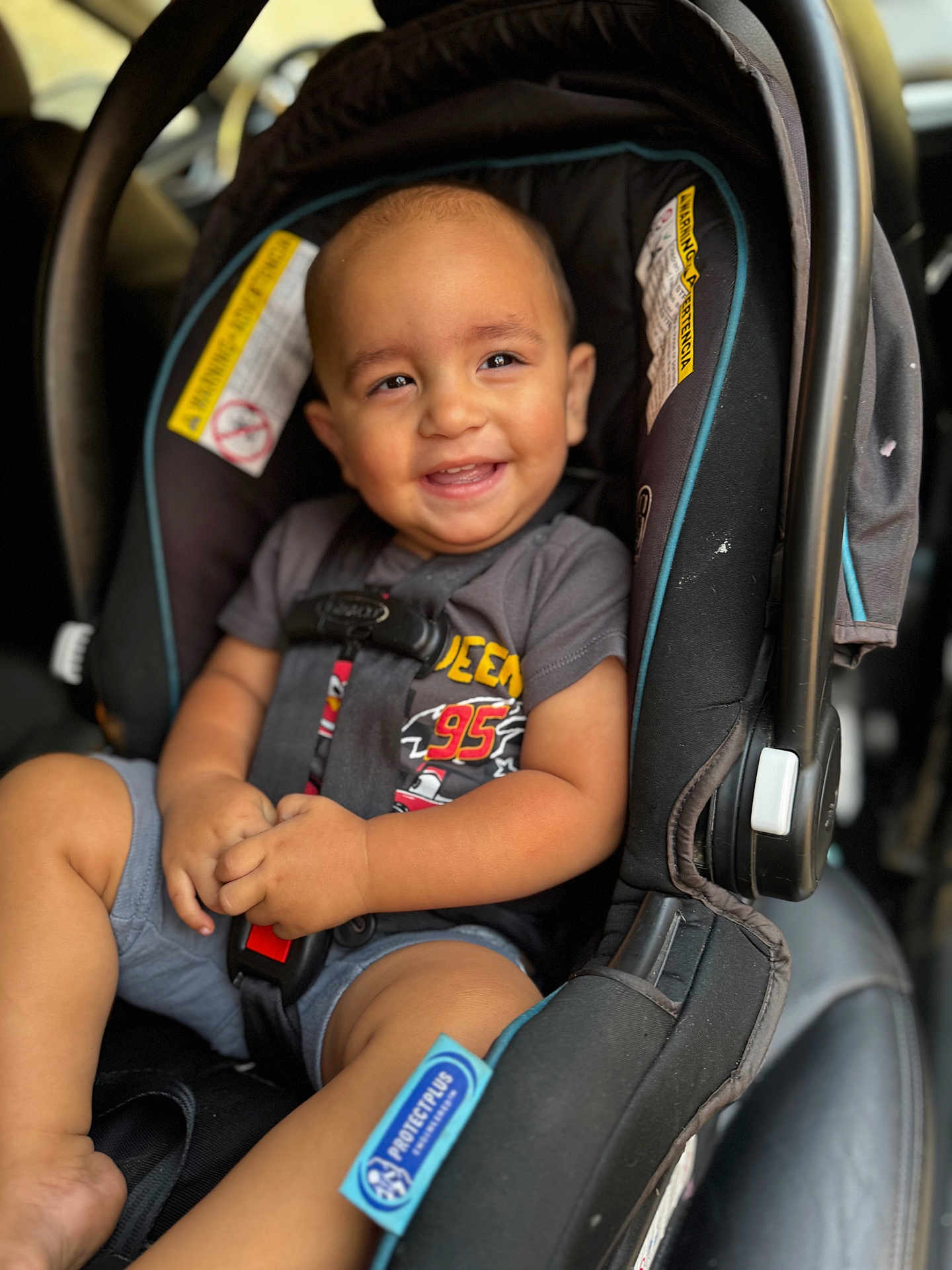 Ezra is registered to the contest to win money with this photo: child, toddler, car_seat, smiling, happy, seatbelt, baby, clothing, shorts, shirt, car_interior, safety, cute, portrait, infant, young_child, seat, strapped_in, automobile, baby_boy
