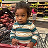 child, toddler, baby, portrait, shopping_cart, supermarket, grocery_store, produce, vegetables, fruit, sitting, curly_hair, striped_shirt, facial_expression, indoors, shopping, cart, store_aisle, background_shopper, family_outing
