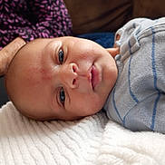 Charles is registered to the contest to win money with this photo: baby, infant, face, skin, blue_eyes, blanket, clothing, striped, soft_texture, portrait, close_up, lying_down, child, young, indoors, person, head, expressionless, cozy, background_blur