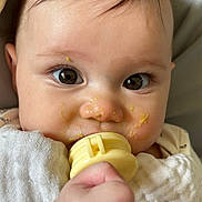 Harper is registered to the contest to win money with this photo: baby, blanket, cheek, close_up, cute, eyelashes, eyes, face, food_on_face, gaze, hand, indoors, infant, messy_food, onesie, pacifier, portrait, skin, teether, toddler