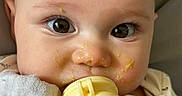Harper is registered to the contest to win money with this photo: baby, blanket, cheek, close_up, cute, eyelashes, eyes, face, food_on_face, gaze, hand, indoors, infant, messy_food, onesie, pacifier, portrait, skin, teether, toddler