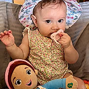 Harper is registered to the contest to win money with this photo: baby, child, pacifier, hat, floral_pattern, plush_doll, indoor, couch, clothing, person, cute, infant, smiling, toy, seated, colorful, face, hand, happy, portrait