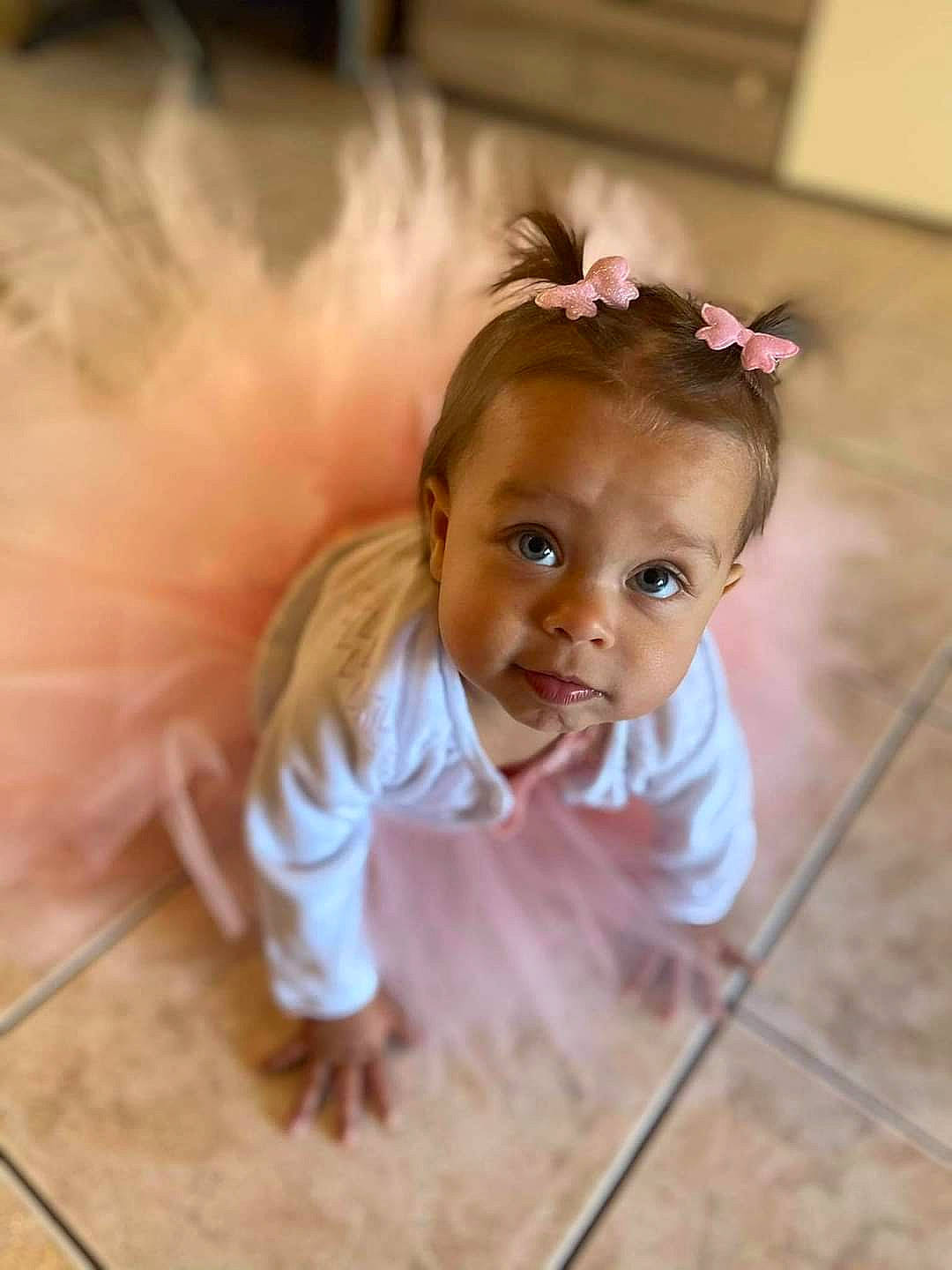 Evy a rejoint le concours — aidez-le/la à gagner de superbes lots ! baby, baby_toddler_clothing, cheek, eye, eyelash, facial_expression, fawn, floor, flooring, hair_accessory, happy, hardwood, headgear, headpiece, iris, person, petal, pink, smile, toddler