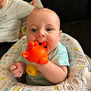 Jason is registered to the contest to win money with this photo: baby, toy, giraffe, orange, baby_seat, couch, adult, indoor, child, chewing, patterned, clothing, person, face, hand, happy, cute, infant, play, comfort