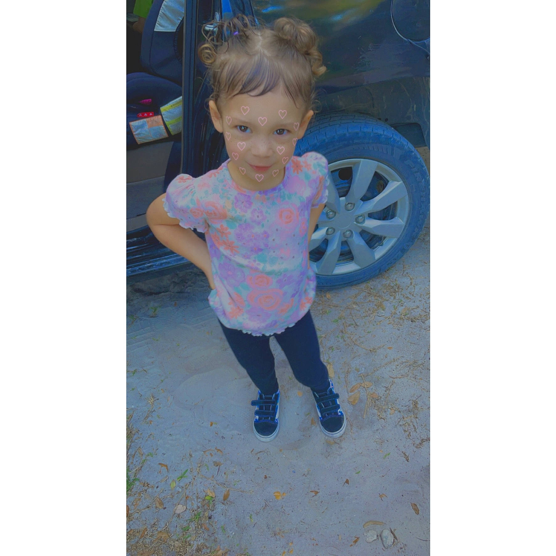 Everly is registered to the contest to win money with this photo: asphalt, automotive_tire, baby_toddler_clothing, bumper, car, denim, electric_blue, footwear, happy, jeans, leg, magenta, person, sleeve, standing, t_shirt, tire, toddler, tree, vehicle_door