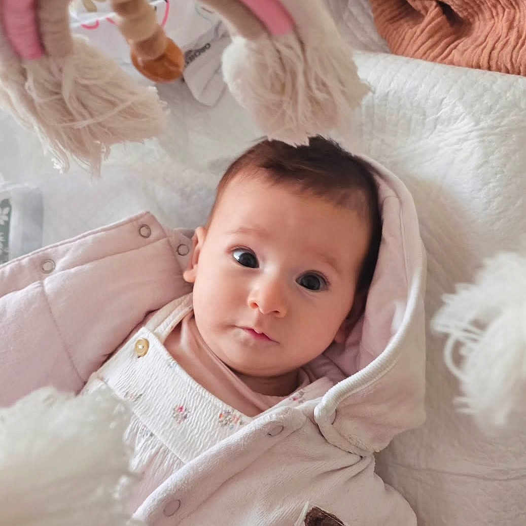 June participe au concours pour gagner de l'argent avec cette photo : baby, bed, blanket, child, childrens_clothing, cozy, cute, eyes, face, hooded_clothing, indoor, infant, pink_jacket, portrait, quilt, rainbow_toy, soft_toy, teddy_bear_patch, toy, warm