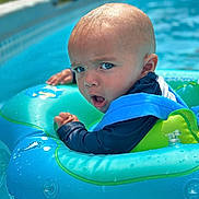 Robert is registered to the contest to win money with this photo: baby, child, pool, water, inflatable_ring, blue, green, floating, summer, outdoor, swimming, cute, expression, face, person, skin, head, eyes, sleeves, fun