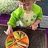 toddler, child, food, fruit, grape, kiwi, pineapple, celery, cheese, sandwich, plate, table, bib, green, indoor, meal, healthy, snack, curly_hair, person
