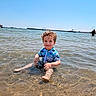 child, toddler, water, beach, sea, sky, sunlight, swimsuit, curly_hair, smile, sitting, shallow_water, sand, outdoor, summer, happy, person, nature, vacation, play