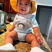 Omar joined the competition — help win amazing prizes! baby, child, infant, smiling, happy, portrait, sun_hat, overalls, rainbow, shoes, kitchen, countertop, indoors, sitting, fashion, cute, face, person, home, photography