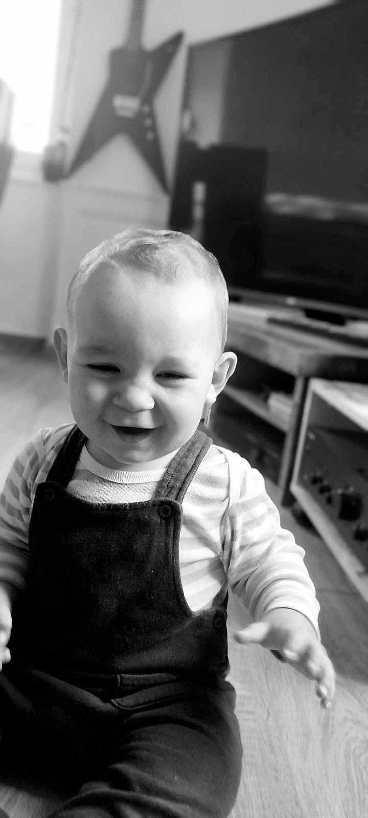 Shelby participe au concours pour gagner de l'argent avec cette photo : toddler, child, smiling, indoor, striped_clothes, overalls, floor, living_room, guitar, television, furniture, black_and_white, portrait, happy, cute, person, home, expression, baby, young_child