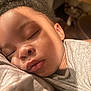 child, sleeping, close_up, face, peaceful, soft_light, shadow, indoors, portrait, young_child, curly_hair, relaxed, tender, skin, person, candid, resting, gentle, warm_tone, quiet