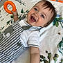 Elio a rejoint le concours — aidez-le/la à gagner de superbes lots ! baby, blanket, cheerful, child, cute, face, happy, head, indoor, infant, lying_down, orange_ring, patterned_blanket, person, playful, smiling, striped_overalls, toy, white_shirt, young_child