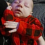 baby, sleeping, infant, red_clothing, checkered_pattern, hand, face, closed_eyes, cozy, child, person, portrait, indoor, rest, cute, newborn, soft_lighting, peaceful, holding, toddler