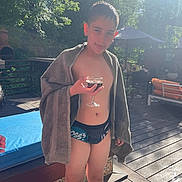 Matthias participe au concours pour gagner de l'argent avec cette photo : boy, child, towel, swimming_pool, outdoor, sunlight, glass, drink, tongue, playful, summer, deck, furniture, trees, greenery, swimwear, person, daylight, relaxation, poolside