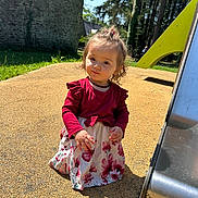 Kaly participe au concours pour gagner de l'argent avec cette photo : child, curly_hair, daylight, dress, floral_dress, girl, grass, necklace, outdoor, playground, portrait, rubber_safety_surface, shadow, slide, smile, squat, stone_wall, sunlight, toddler, trees