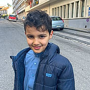 Amir participe au concours pour gagner de l'argent avec cette photo : child, boy, smile, jacket, blue_clothing, urban, street, car, building, sidewalk, daylight, portrait, person, standing, casual, outdoor, young, happy, face, hair