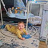 baby, child, infant, smiling, happy, indoor, playroom, jumper, baby_gear, toy, yellow_outfit, rug, carpet, home, furniture, air_conditioner, crib, portrait, sitting, playtime