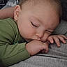 baby, blanket, child, closed_eyes, couch, cozy, face, gray_blanket, green_clothing, hand, home, indoors, infant, light_hair, peaceful, portrait, remote_control, resting, sleeping, soft_texture