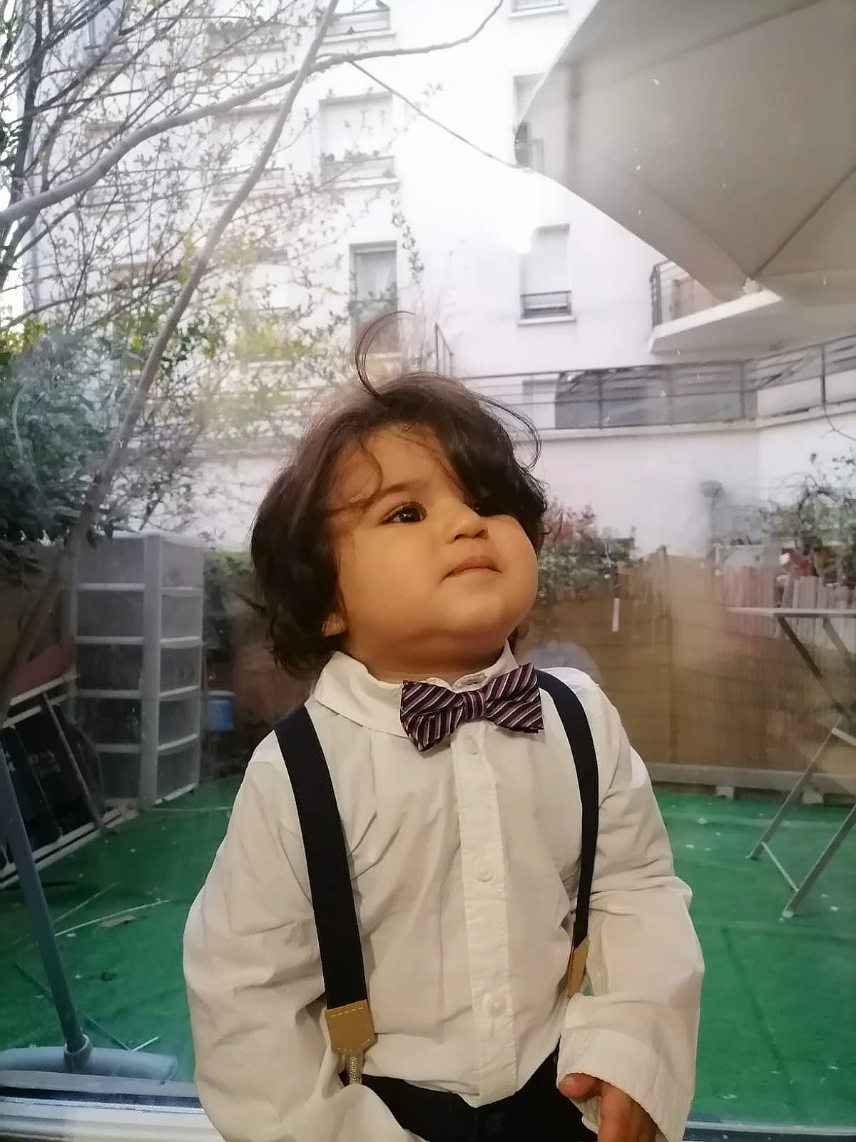 Mohamed participe au concours pour gagner de l'argent avec cette photo : black_hair, building, chair, child, collar, costume, dress_shirt, flooring, formal_wear, fun, person, plant, school_uniform, sitting, sky, sleeve, street_fashion, toddler, tree, uniform