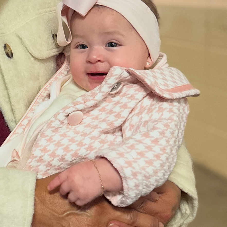 Ariathna is registered to the contest to win money with this photo: adult_hands, baby, blurred_background, bokeh, bow, bracelet, cheeks, coat, earring, fire_extinguisher, hands, headband, holding, houndstooth, indoor, infant, pink, portrait, ring, smile