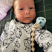 Gregory is registered to the contest to win money with this photo: baby, infant, onesie, sheep_pattern, pacifier, blanket, face, expression, lying_down, soft_toys, cute, child, indoors, close_up, newborn, sleepwear, comfort, adorable, person, young