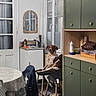 books, bottle, brown_and_white_dog, cabinet, chair, dining_area, dog, furniture, home, indoors, kitchen, mirror, pet_bowl, portrait, sitting, table, tablecloth, tissues, window, wooden_floor