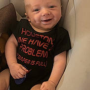 Greysen joined the competition — help win amazing prizes! baby, infant, child, smiling, happy, portrait, face, sitting, indoor, cushion, chair, black_shirt, text_on_clothing, red_lettering, bald, eyes, hands, arms, legs, cozy