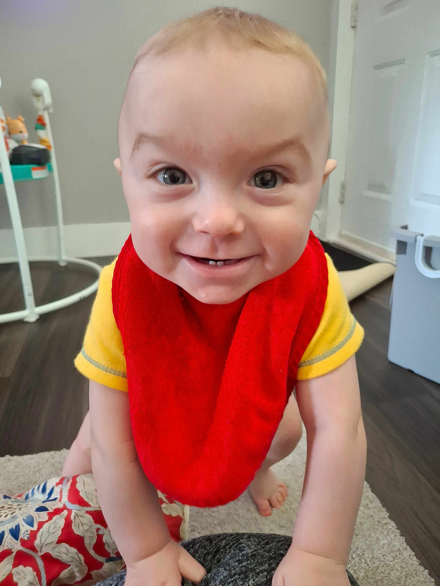 Marley joined the competition — help win amazing prizes! baby, child, smiling, red_bib, yellow_shirt, crawling, indoor, floor, carpet, toy, face, person, happy, young_child, home, light_skin, cute, expression, closeup, infant