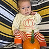 Augustus joined the competition — help win amazing prizes! baby, child, infant, portrait, sitting, pumpkin, autumn, sweater, striped_pants, socks, blanket, textile, yellow, orange, black, white, indoor, baby_clothing, blue_eyes, harvest
