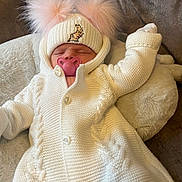 Rayah-Rose is registered to the contest to win money with this photo: baby, infant, sleeping, knitted_clothing, white_outfit, hat, pom_poms, pacifier, pink, plush_cushion, cozy, cute, child, resting, indoor, soft_texture, warm, newborn, person, portrait