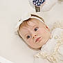 baby, infant, child, portrait, headband, bow, white_clothing, frills, earrings, blue_eyes, soft_lighting, closeup, lying_down, curious_expression, indoor, cute, adorable, face, skin, person