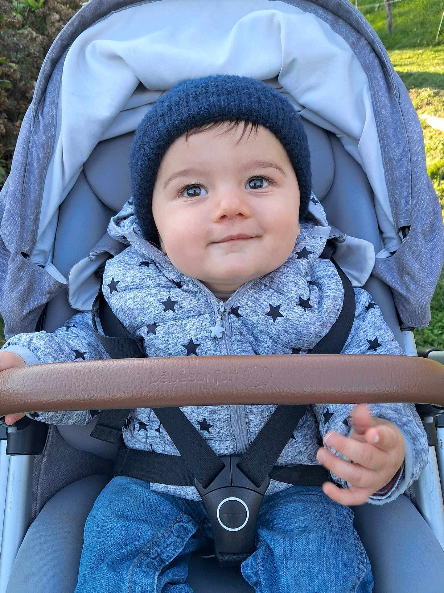 Sacha participe au concours pour gagner de l'argent avec cette photo : baby, child, stroller, jacket, hat, knit_hat, star_pattern, smile, face, hand, safety_harness, outdoor, grass, cushion, clothing, person, infant, seat, happy, cute