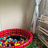 cat, black_and_white_cat, pet, animal, sleeping, ball_pit, colorful_balls, inflatable_pool, watermelon_design, toy, playroom, children_room, books, shelving, curtains, window, indoor, home, foam_mat, relaxed