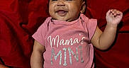 Kaileiah is registered to the contest to win money with this photo: baby, infant, child, smiling, happy, portrait, lying_down, red_blanket, pink_outfit, onesie, sparkly_text, mamas_mini, raised_hand, gummy_smile, indoor, close_up, adorable, fabric, person, family_photo