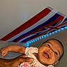 baby, child, infant, smiling, happy, portrait, held, adult_hands, indoor, bedroom, flag, union_jack, blue_lights, led_lights, white_clothing, printed_shirt, heart, close_up, face, family