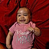 baby, infant, child, smiling, portrait, lying_down, red_blanket, pink_clothing, onesie, gummy_smile, raised_fist, indoor, close_up, happy, dark_background, fabric, baby_fashion, mama, adorable, photography