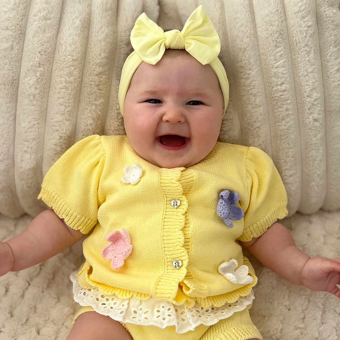 Delilah-Lilly is registered to the contest to win money with this photo: baby, butterfly_applique, buttoned_cardigan, child, chubby_arms, chubby_legs, cozy, cute, happy, headband, headwear, indoors, infant, knitwear, plush_background, portrait, sitting, smiling, soft_texture, yellow_clothing